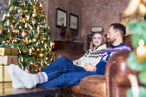 Сouple wearing warm socks and jerseys while sitting on the sofa near Christmas tree