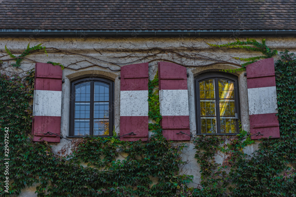 Mittelalterliche Hausfassade mit rot-weiß-roten Fensterläden und Efeu