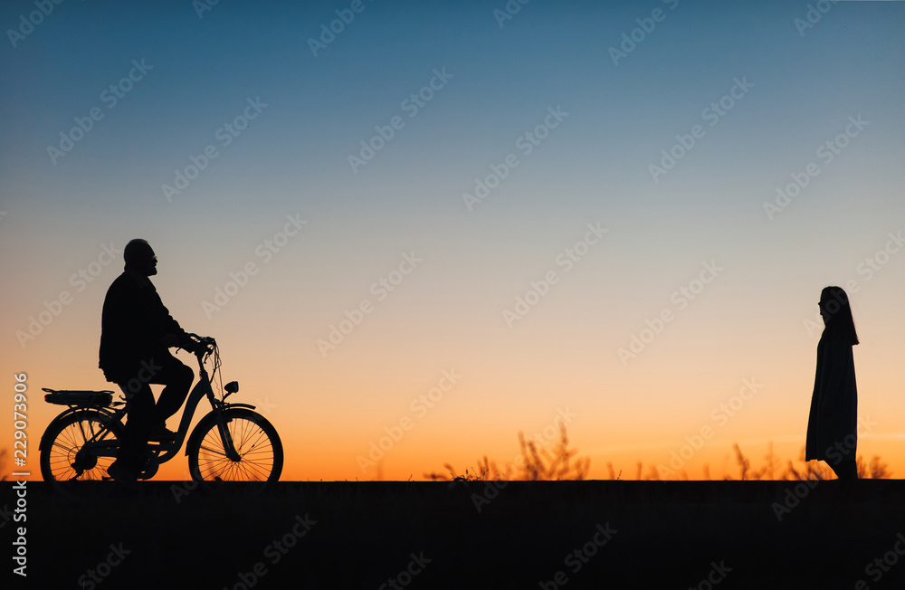 Fototapeta premium Male cyclist on the e-bike or electric bicycle on the sunset background. Silhouette of the man in profile. Active pension. Travel. Sport.