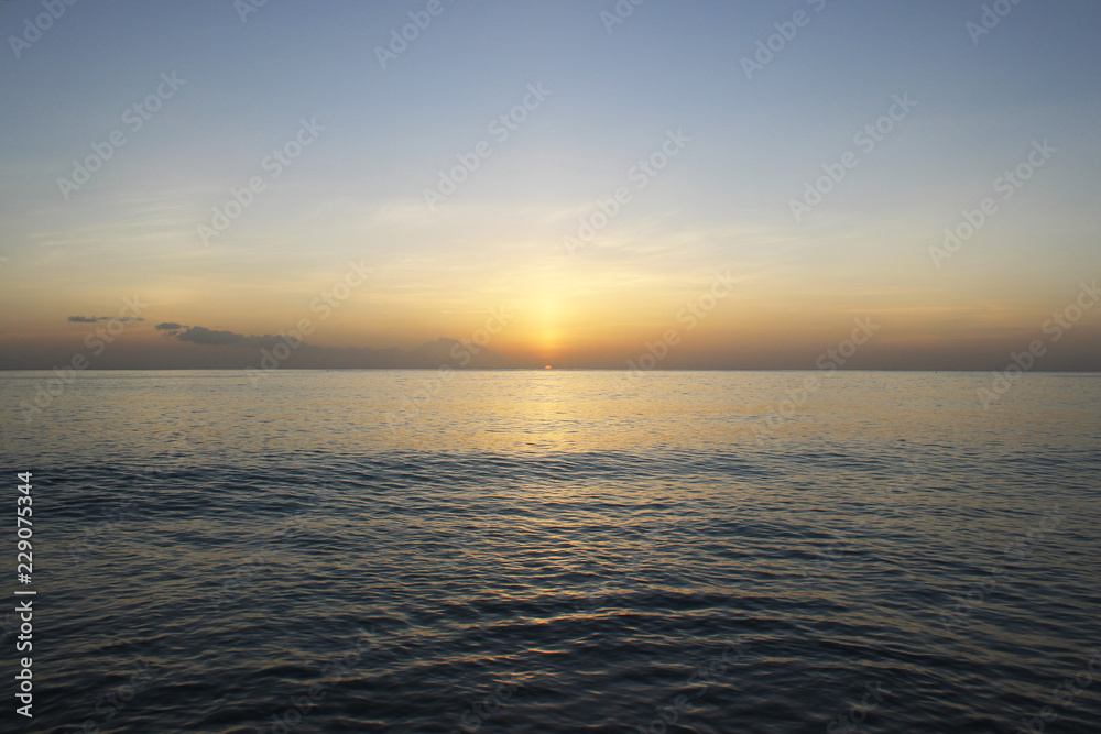Calming and beautiful orange sunset against blue seashore Calming and beautiful orange sunset against blue seashore