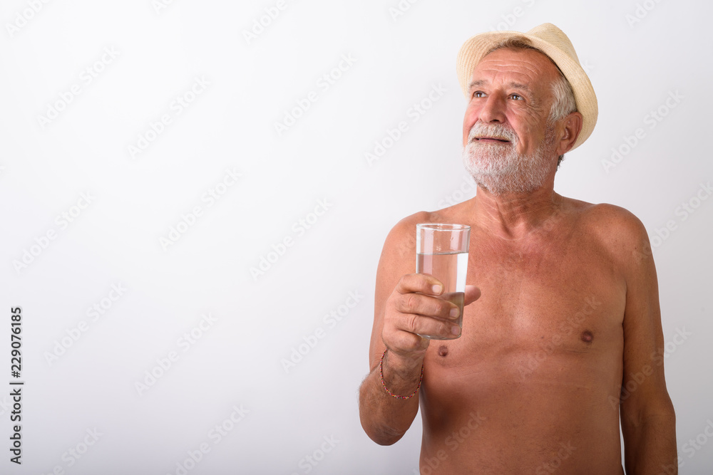Fototapeta premium Shirtless senior man holding glass of water while thinking