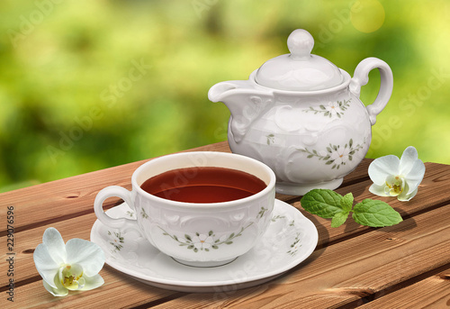 Earl grey / black tea in tea cup and teapot on wooden table and green garden