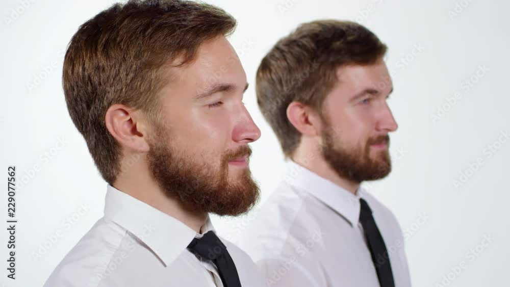 Medium shot of two optimistic twin brothers standing next to each other against white background and looking at distance Medium shot of two optimistic twin brothers standing next to each other against white background and looking at distance