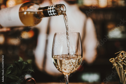 Close up shot of a bartender pouring white wine into a glass. Hospitality, beverage and wine concept. photo