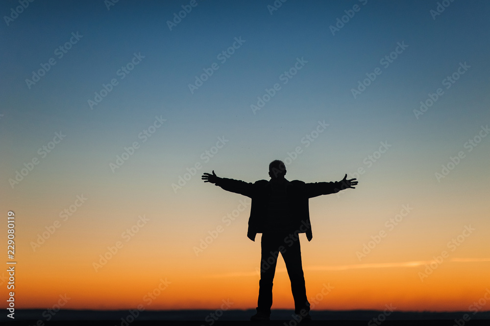 Silhouette of a man spread his arms to the side. Religion, Faith and Prayer. Unity with nature. On the sunset background. Freedom.