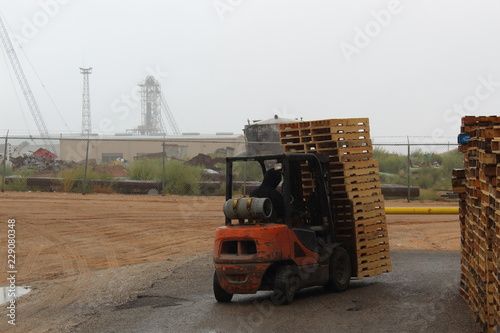 Fork lift driver loading pallets into a warehouse, New wooden pallets on the forks and rain falling from the sky makes it for a interesting time.