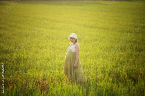 pregnant woman in green dress relaxing in the meadow with sunset