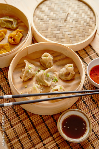 Oriental traditional chinese dumplings served in the wooden steamer placed on bamboo mat. Top View composition.