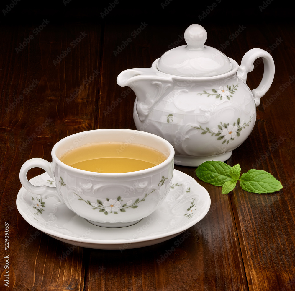 Green tea in porcelain cup and teapot with mint on wooden table Green tea in porcelain cup and teapot with mint on wooden table