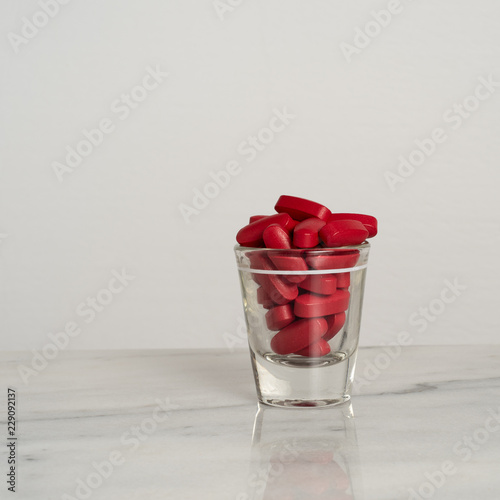 medicine red pills pharmaceutical capsules in small glass cup on granite  surface with white background ideal for medication medical clinic ads treatments morning pills or health related background