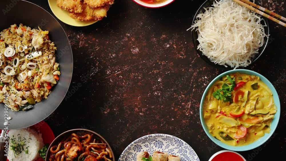 Asian food set. Noodles, fried rice with chicken, tom yum soup, spring rolls, deep fried fish and udon with prawns. Top view on dark rustic background. Oriental style food circle composition.