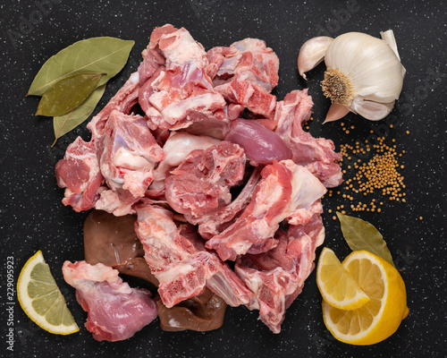 Fresh raw goat meat stew like cuts on black cutting board with spices mustard seeds, garlic, lemon, and bay leaves.