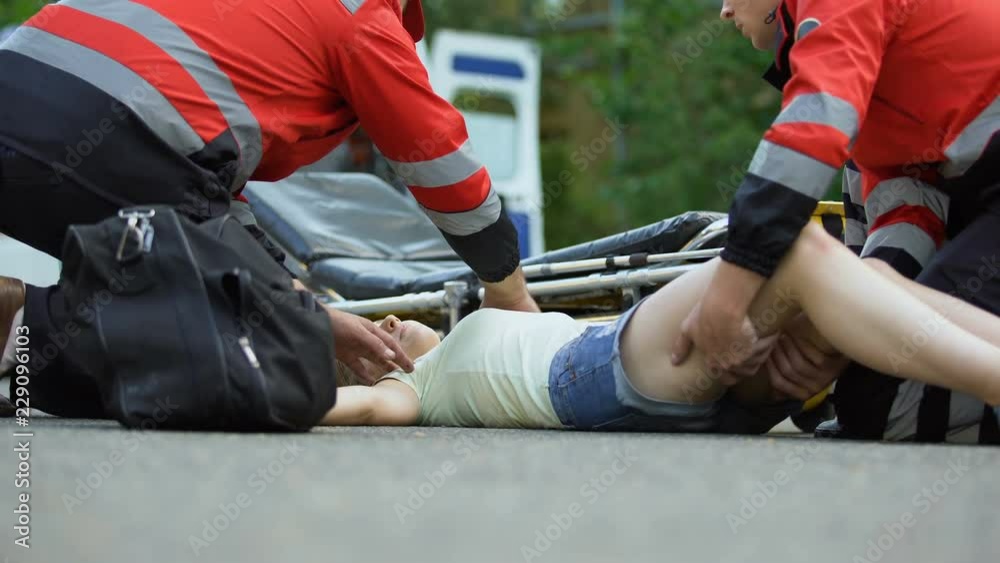Ambulance service staff taking unconscious girl to ambulance, using stretcher