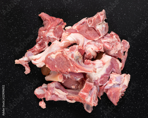 Fresh raw goat meat stew like cuts on black cutting board.