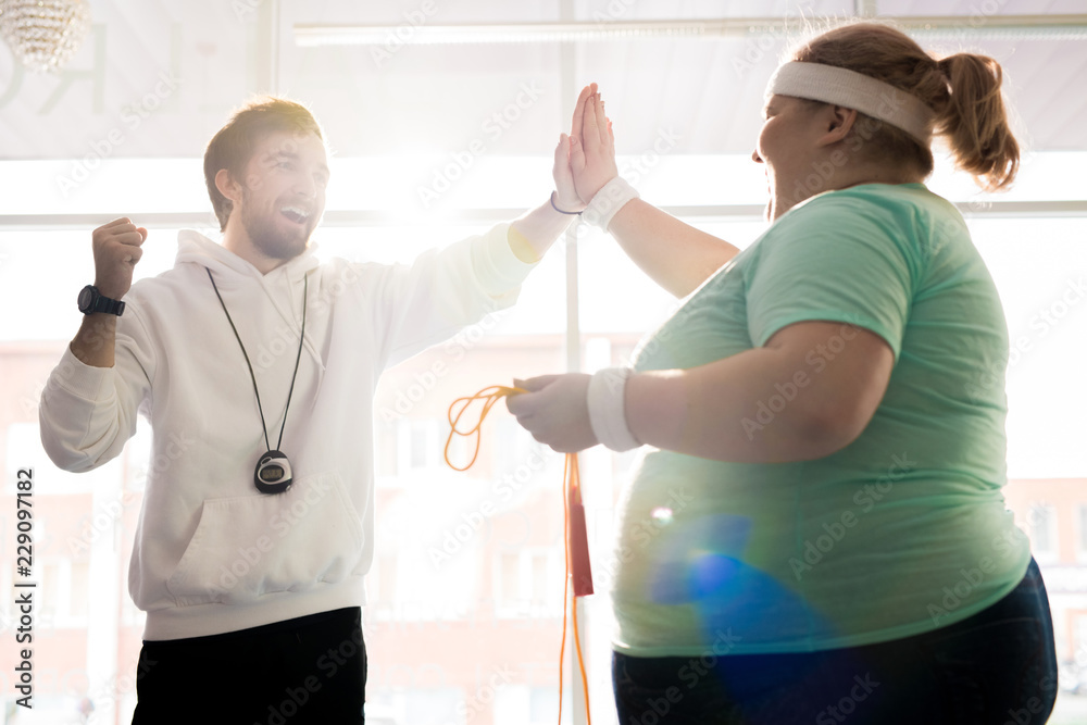 Waist up portrait of smiling fitness coach high fiving with fat young woman during workout in sunlight Waist up portrait of smiling fitness coach high fiving with fat young woman during workout in sunlight