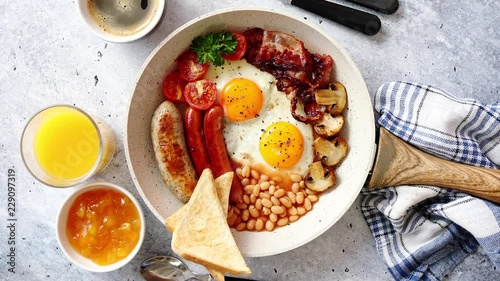 Full English Breakfast served in a pan. Fried eggs, beked beans, tomatoes, champignons, crispy bacon, sausages and toast. Placed on stone background. Top view with copy space. photo