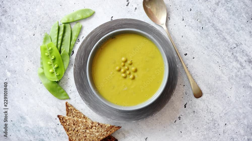 Green pea cream soup in grey bowl placed with spices, fresh peas, full grain bread on stone background. Top view with copy space. Green pea cream soup in grey bowl placed with spices, fresh peas, full grain bread on stone background. Top view with copy space.