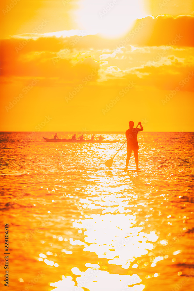 Hawaii ocean lifestyle - watersport activity on ocean - stand up paddleboard, people training on outrigger canoe . Active summer healthy living. Silhouette of standing person doing paddle board.