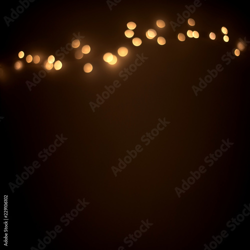 Defocused golden christmas lights on  dark abstract background.  Glowing light bulb garland, copy space