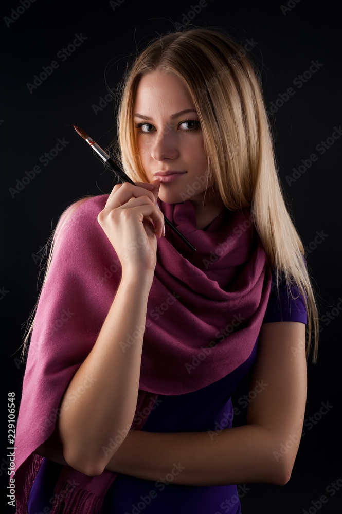 Beautiful young woman holding a paintbrushes over black background
