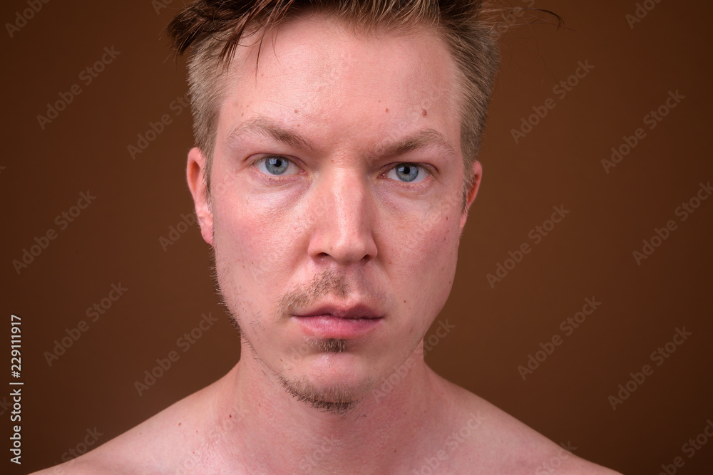 Fototapeta premium Young handsome man shirtless while grooming against brown backgr