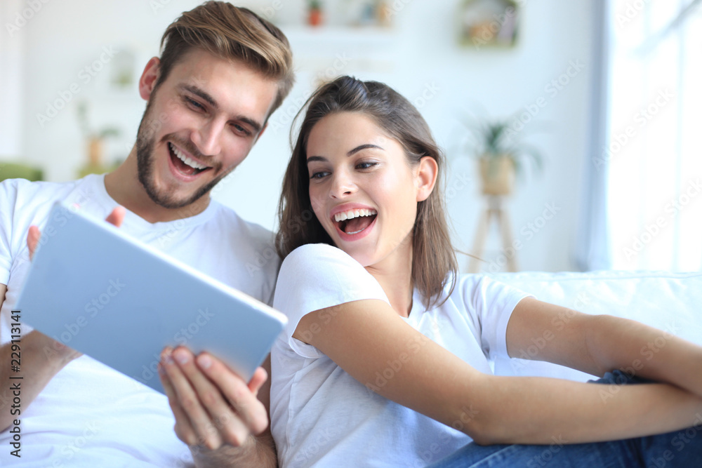 Young couple watching media content online in a tablet sitting on a sofa in the living room. Young couple watching media content online in a tablet sitting on a sofa in the living room.