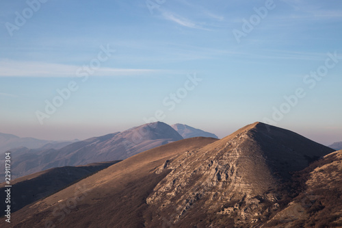 A view of some mountains top, beneath an empty blue sky at golden hour