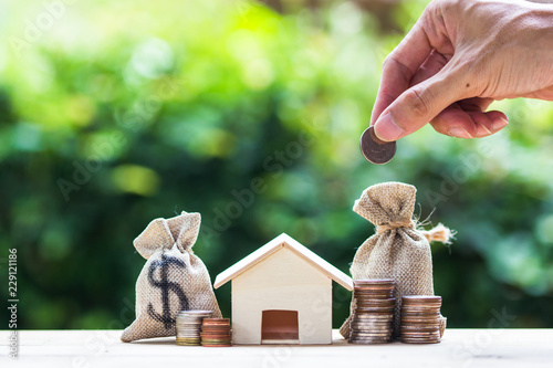 Saving money, home loan, mortgage, a property investment for future concept : A man hand putting money coin over small residence house and money bag. photo
