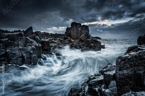 Moody dramatic skies and large waves crash onto coastal rocks
