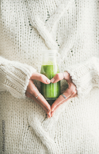 Winter seasonal smoothie drink detox. Female in warm sweater holding bottle of green smoothie or juice making heart shape with her hands. Clean eating, weight loss, healthy dieting food concept