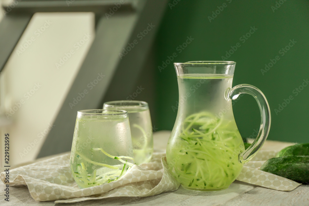 Glassware of fresh cucumber water on light wooden table