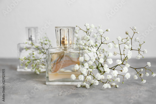 Transparent bottle of perfume with beautiful flowers on grey table