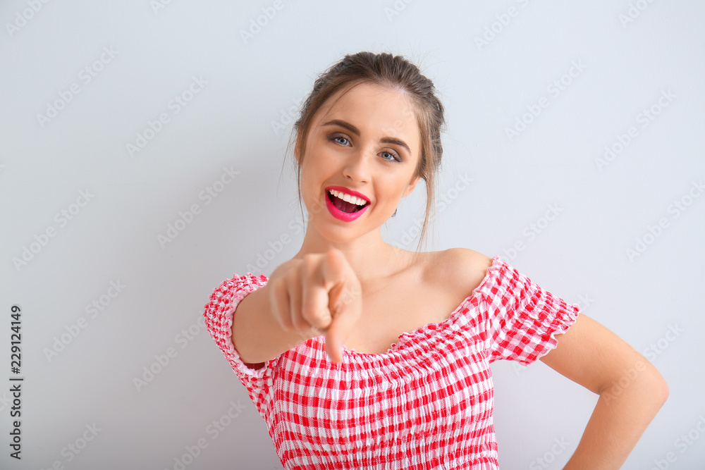 Beautiful young woman pointing at viewer on light background Beautiful young woman pointing at viewer on light background
