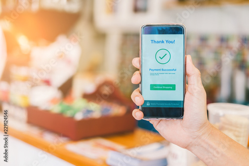 Hand holding smartphone showing payment successful transaction at department store or coffee shop, Cashless technology concept photo