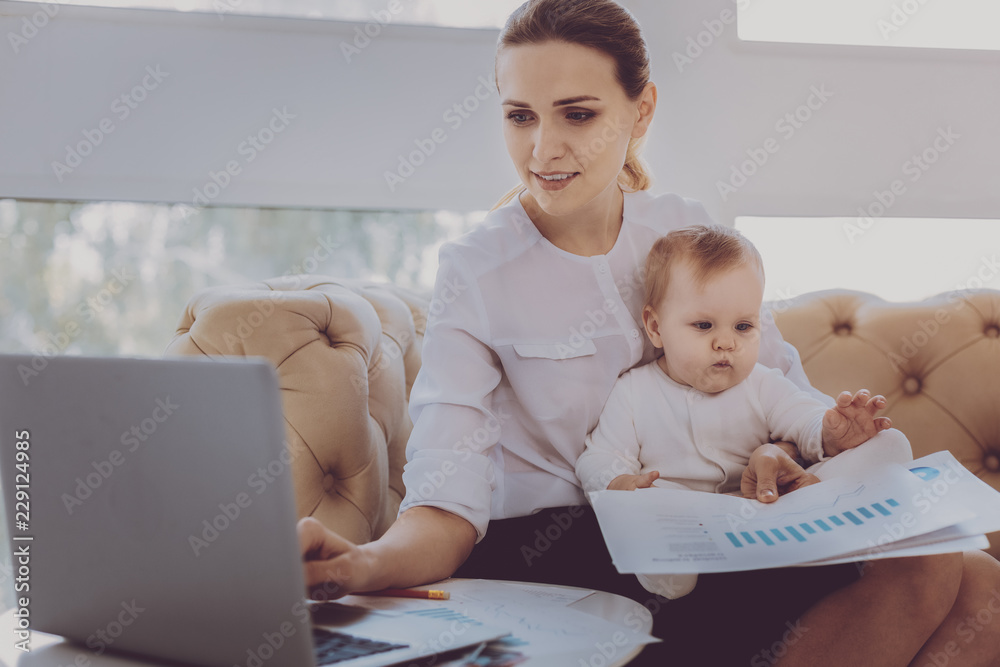 Maternity leave. Fashion designer on maternity leave feeling motivated checking her e-mail while holding little sweet baby Maternity leave. Fashion designer on maternity leave feeling motivated checking her e-mail while holding little sweet baby