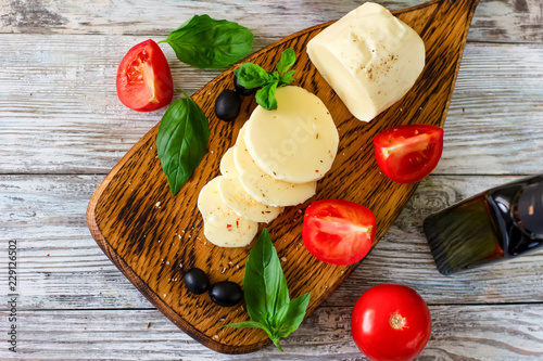 Mozzarella cheese with tomatoes and Basil on wooden background, top view