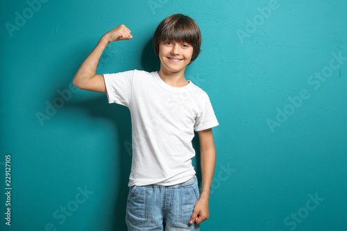 Little boy in t-shirt showing muscles on color background photo