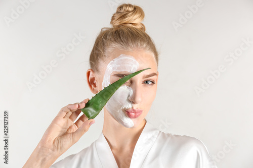 Beautiful young woman with facial mask containing aloe vera extract, on light background