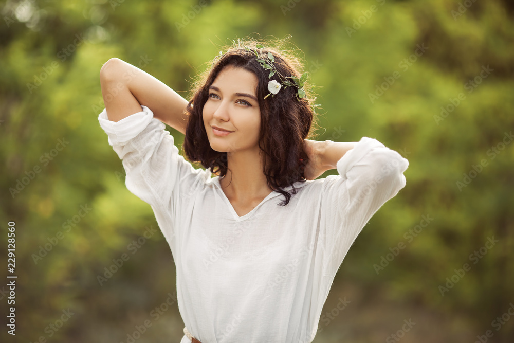 Beauty woman portret on nature. Beautiful young lady standing on wheat fields during sunset, wear summer white dress and head flower wreath. Attractive young girl outdoor.