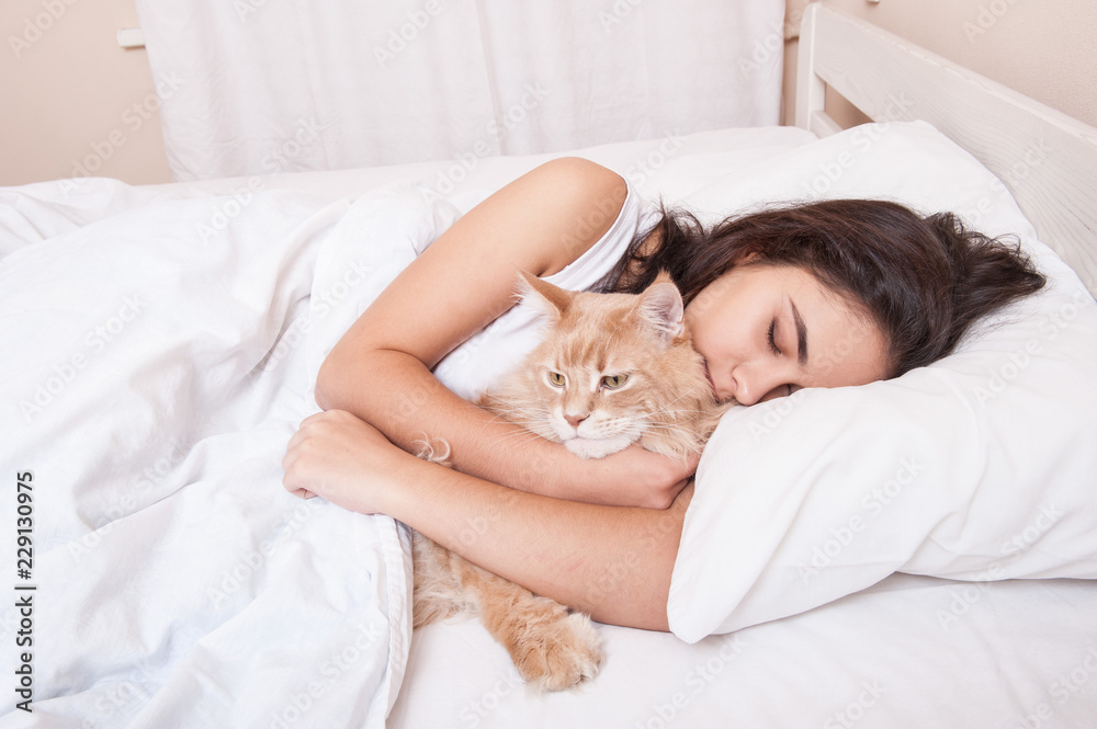 The girl is sleeping in the bed with the cat maine coon The girl is sleeping in the bed with the cat maine coon