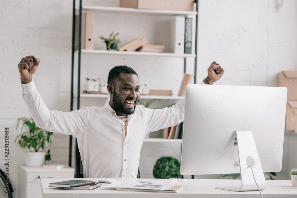 happy african american businessman working at computer in office and showing yes gesture