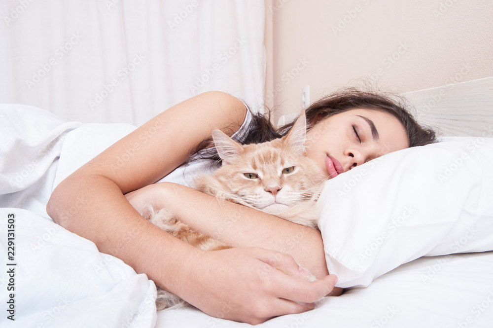 The girl is sleeping in the bed with the cat maine coon The girl is sleeping in the bed with the cat maine coon
