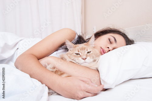 The girl is sleeping in the bed with the cat maine coon