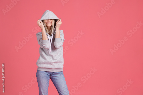 Girl closing her eyes with a hood smiles and standing on a bright pink background. Place to advertise