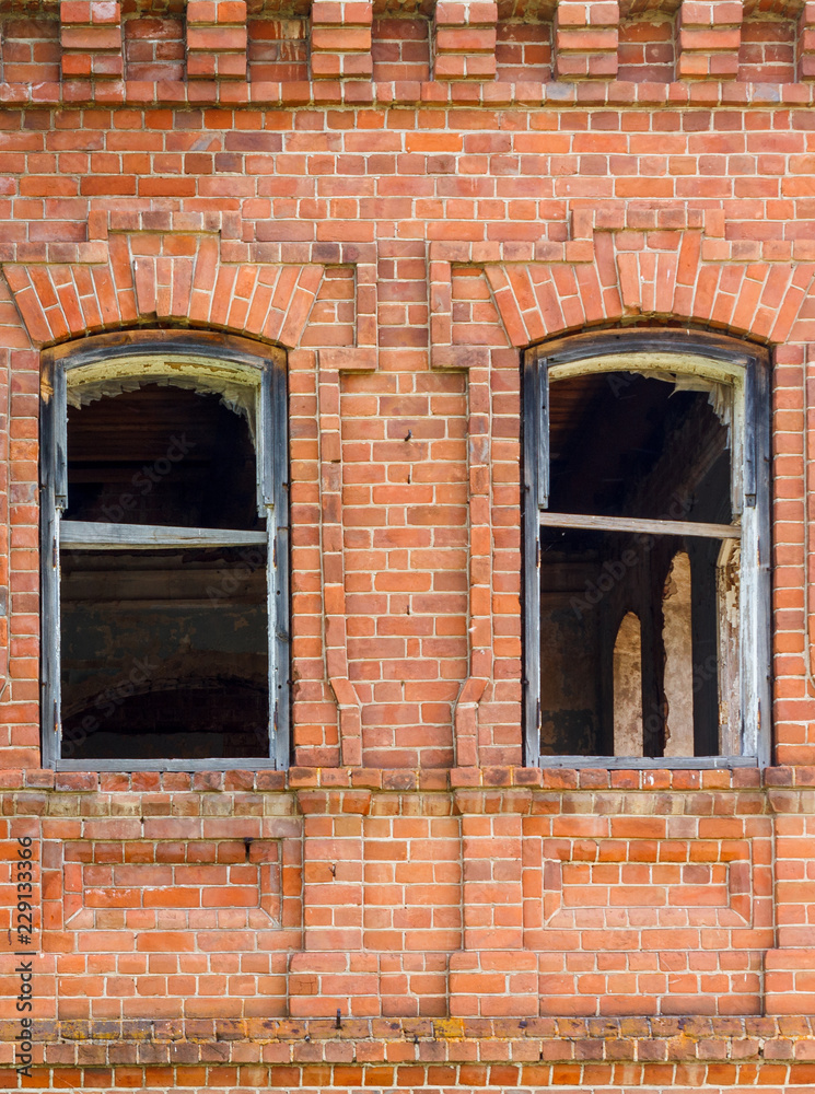 Two windows of an old destroyed building made of red brick, through which you can see the dark ruined rooms.