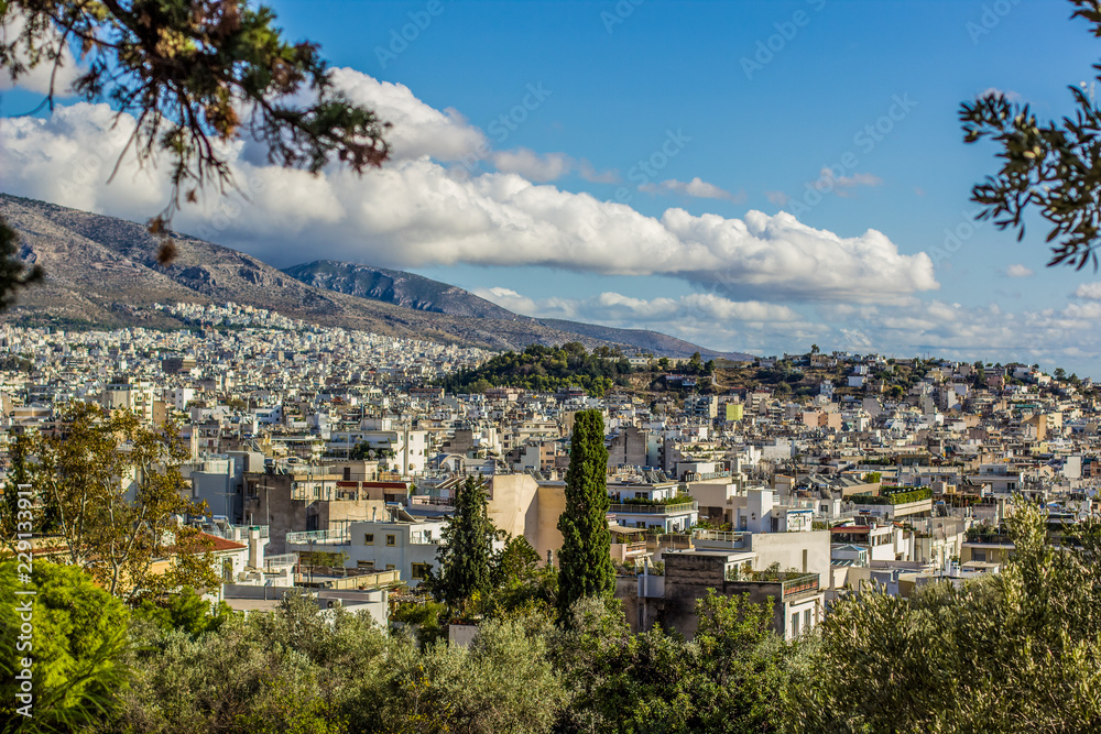 Athens city view of capital of Greece from hill top and foreshortening between trees branches to many buildings, mountain and blue sky with clouds