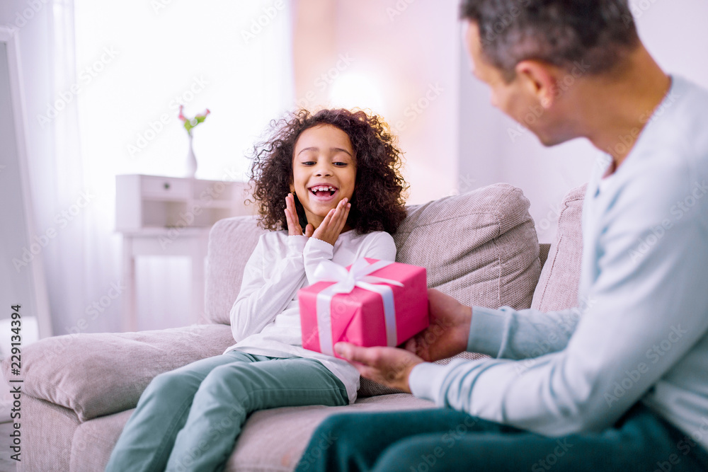 Happy birthday. Pleased brunette girl keeping smile on her face while looking at gift box Happy birthday. Pleased brunette girl keeping smile on her face while looking at gift box