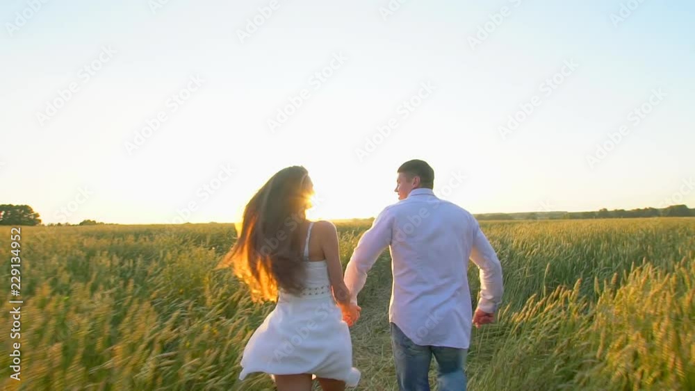 Happy young couple holding hands and runing through wheat field at summer sunset, having fun outdoors. Countryside, summer time. Man and woman, happy family in love. Nature. Sun flare Slow motion Happy young couple holding hands and runing through wheat field at summer sunset, having fun outdoors. Countryside, summer time. Man and woman, happy family in love. Nature. Sun flare Slow motion