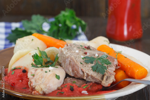 Boiled beef and chicken meat with creamy tomato sauce served with potatoes, carrots, dill and celery. Homemade cuisine, wooden background.