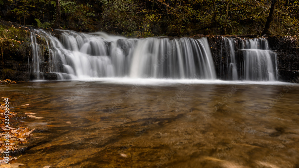 Waterfall Ddwli Isaf near pontneddfechan in the brecon beacons national park, Wales. It is autumn, and golden leaves are all around.  Long shutter speed for a smooth effect on the water